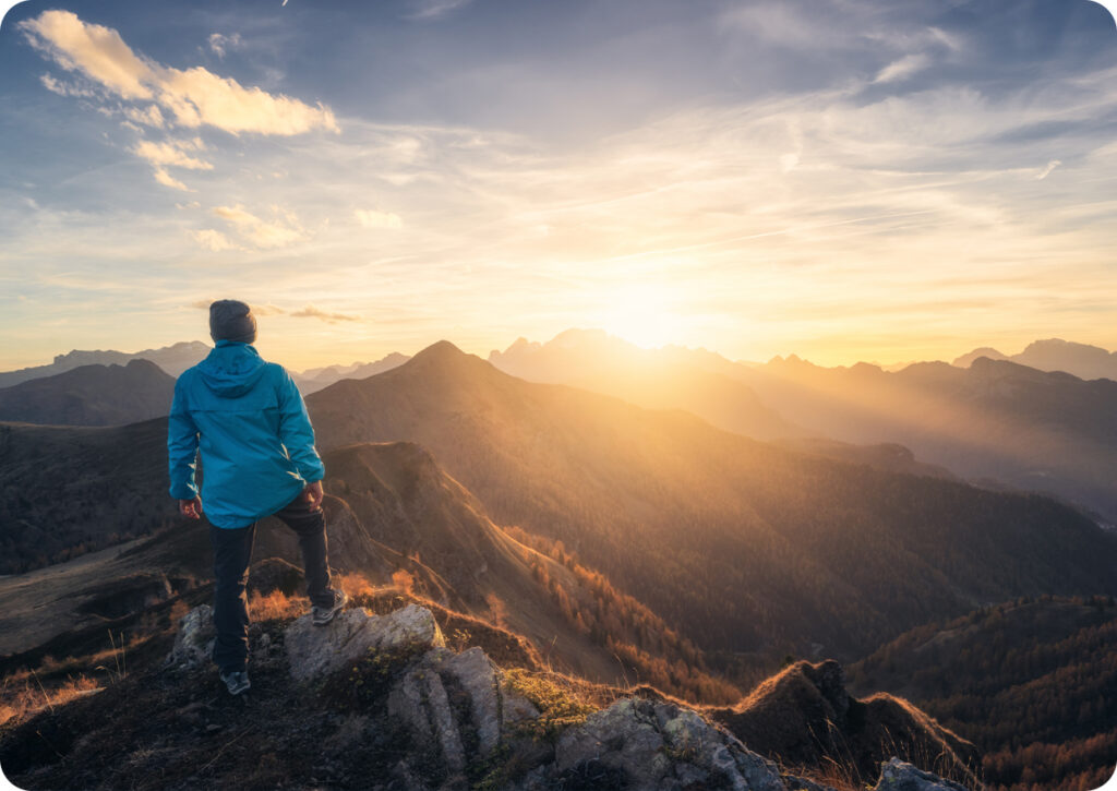 brand-identity-two-col-img-2 | HIFI Agency | Financial Marketing Agency Hiker in a blue jacket stands on rocky ridge watching a sunrise over rugged mountains.