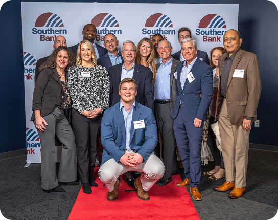 Group of twelve professionals posing on a red carpet at a Southern Bank event, in front of a backdrop with the bank's logo.