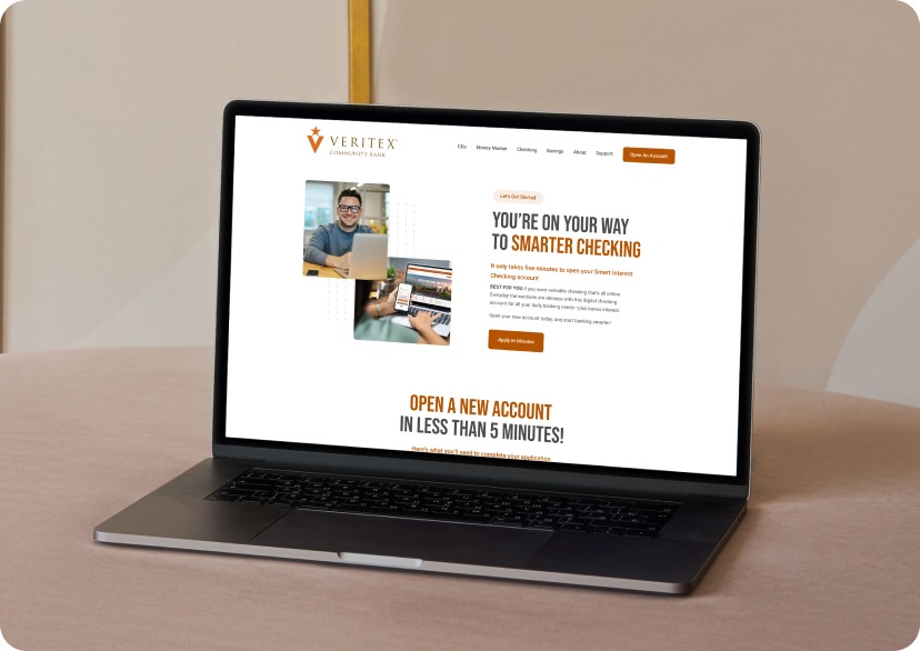 Laptop on a wooden desk showing the Veritex Community Bank website with orange headings and a photo collage on the screen, including a man using a laptop and a city image.