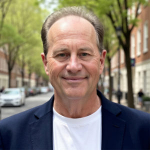 Smiling man in a navy blazer and white shirt standing on a tree-lined city street with buildings in the background.